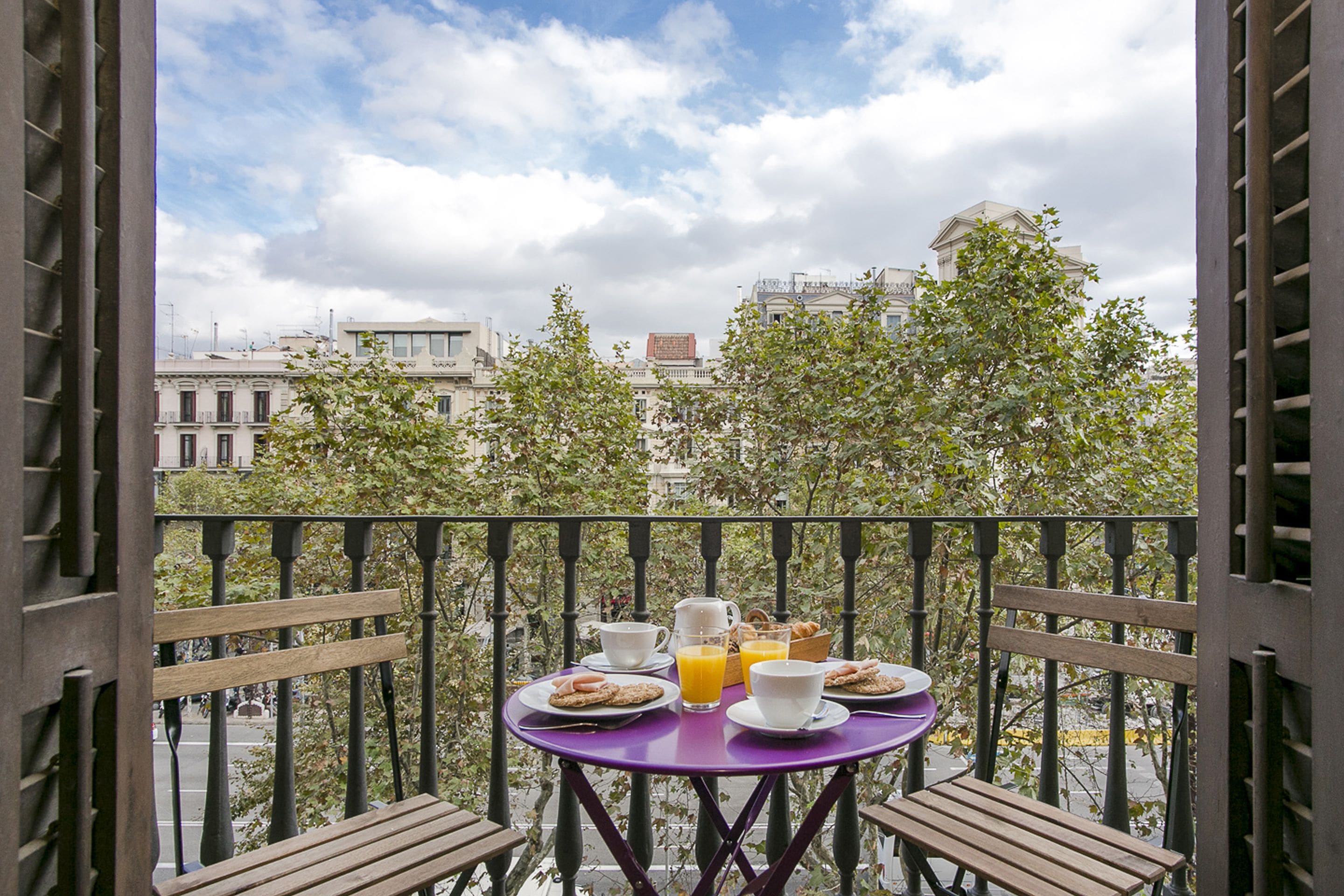 A balcony with a purple table set for breakfast, including plates, cups, and orange juice.