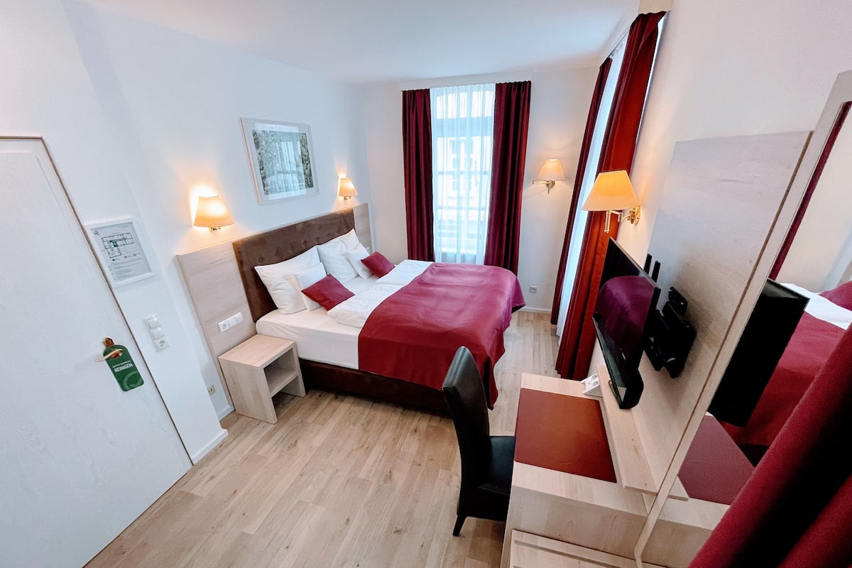 A hotel room with a bed, bedside tables, a desk, a chair, a TV, and a mirror.