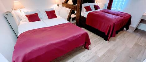 Quarto com duas camas, vigas de madeira, paredes brancas e uma janela com cortinas.