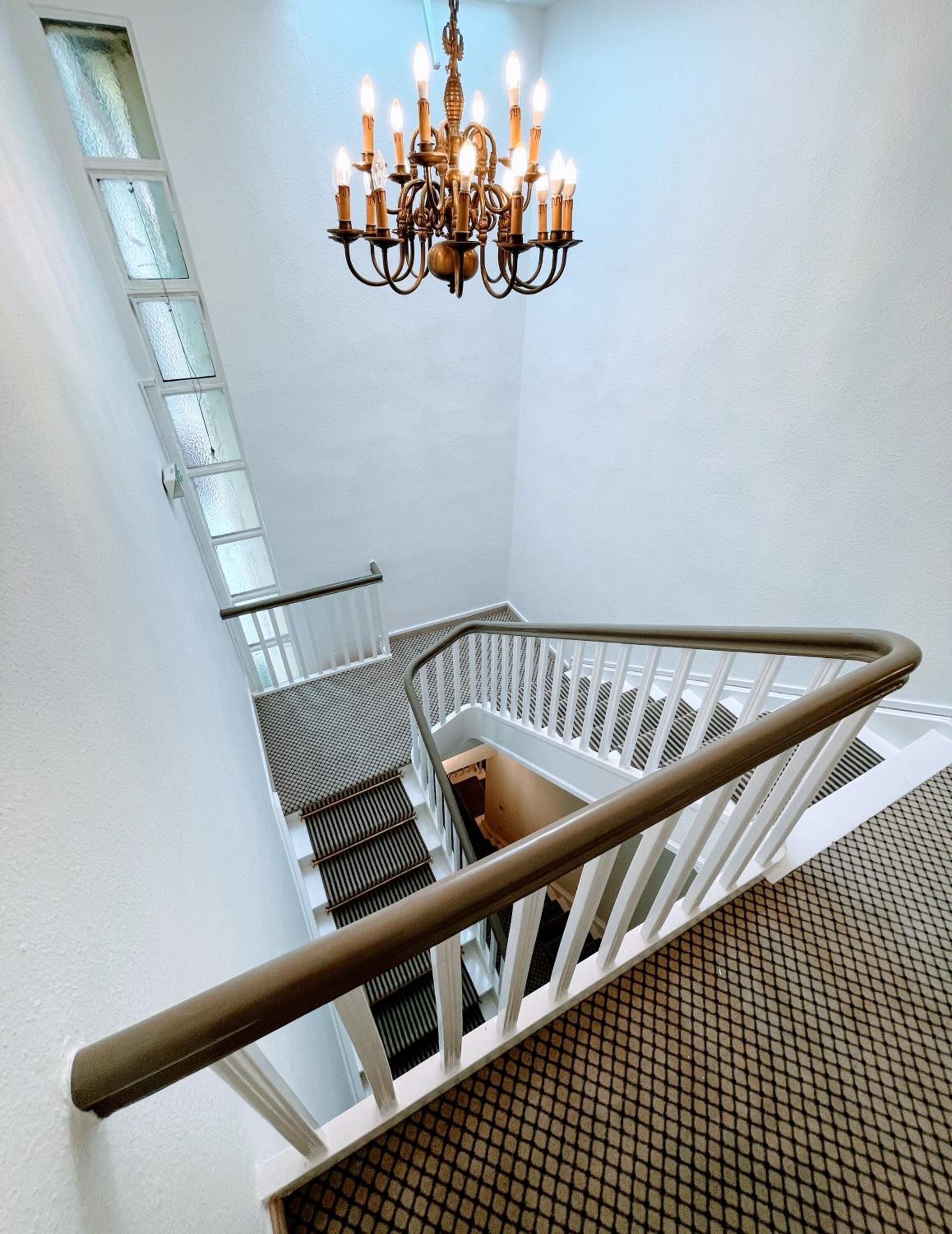 Un escalier avec une rampe métallique, un lustre et une fenêtre avec des panneaux de verre dépoli.
