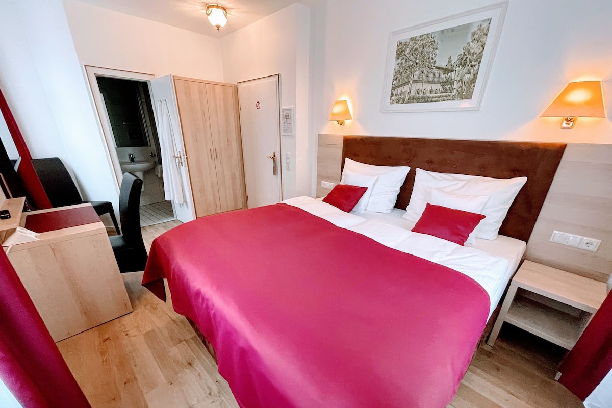 A hotel room with a bed, bedside tables, a desk, and a wardrobe.