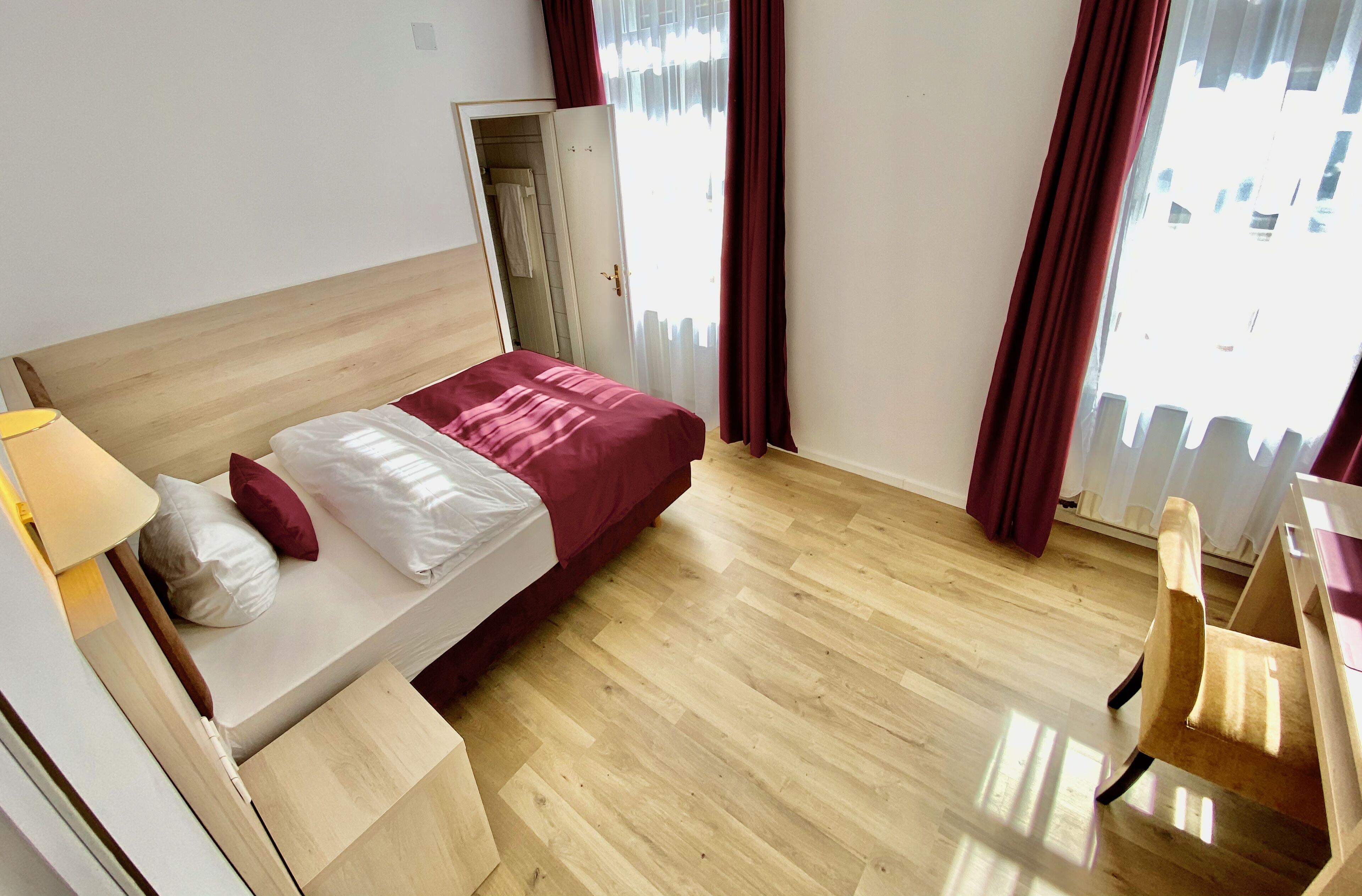 Une chambre d’hôtel avec un lit, un bureau, une chaise et une fenêtre avec des rideaux.