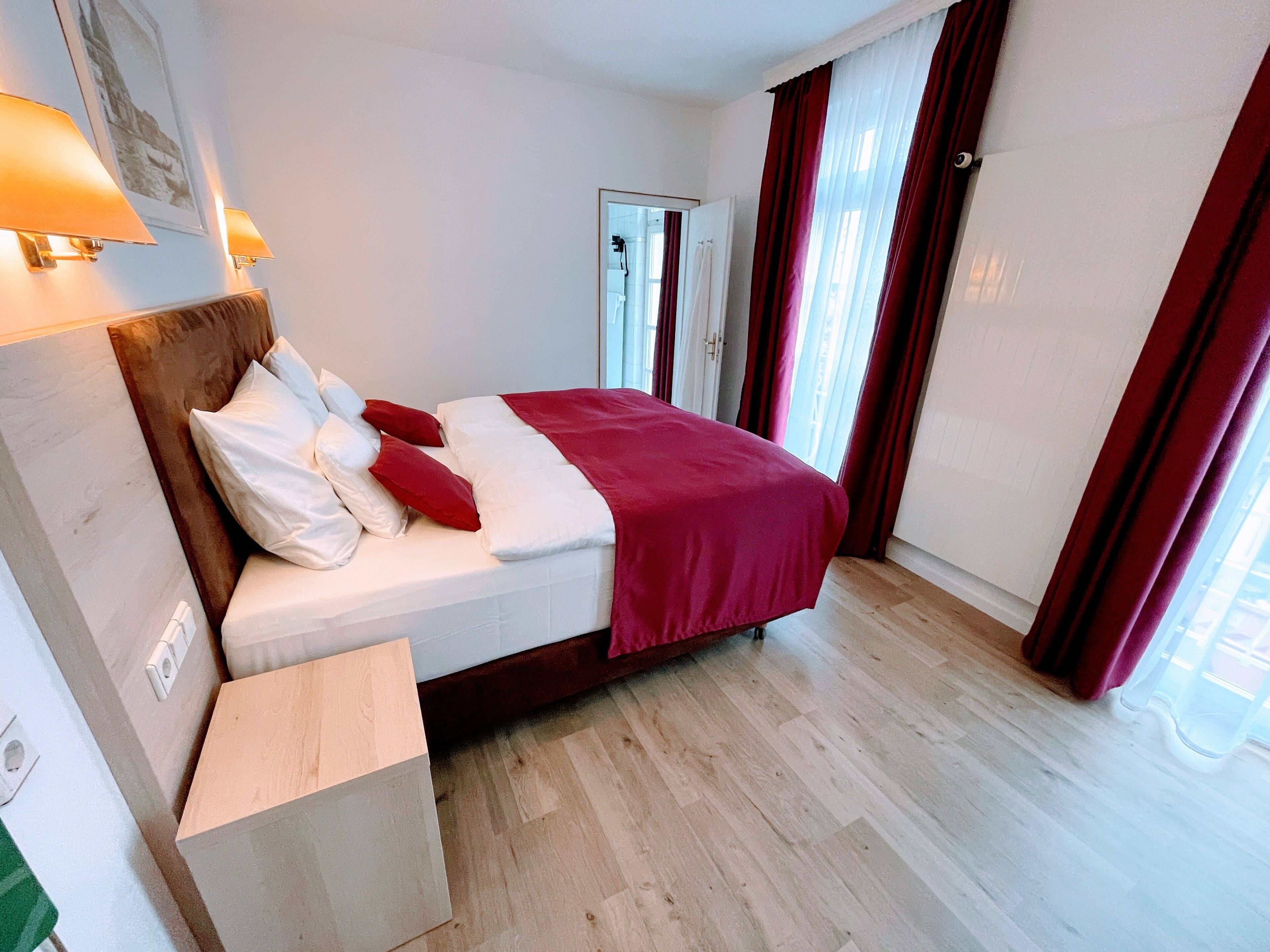 Ein ordentlich eingerichtetes Hotelzimmer mit Bett, Nachttisch, Spiegel und Tür.