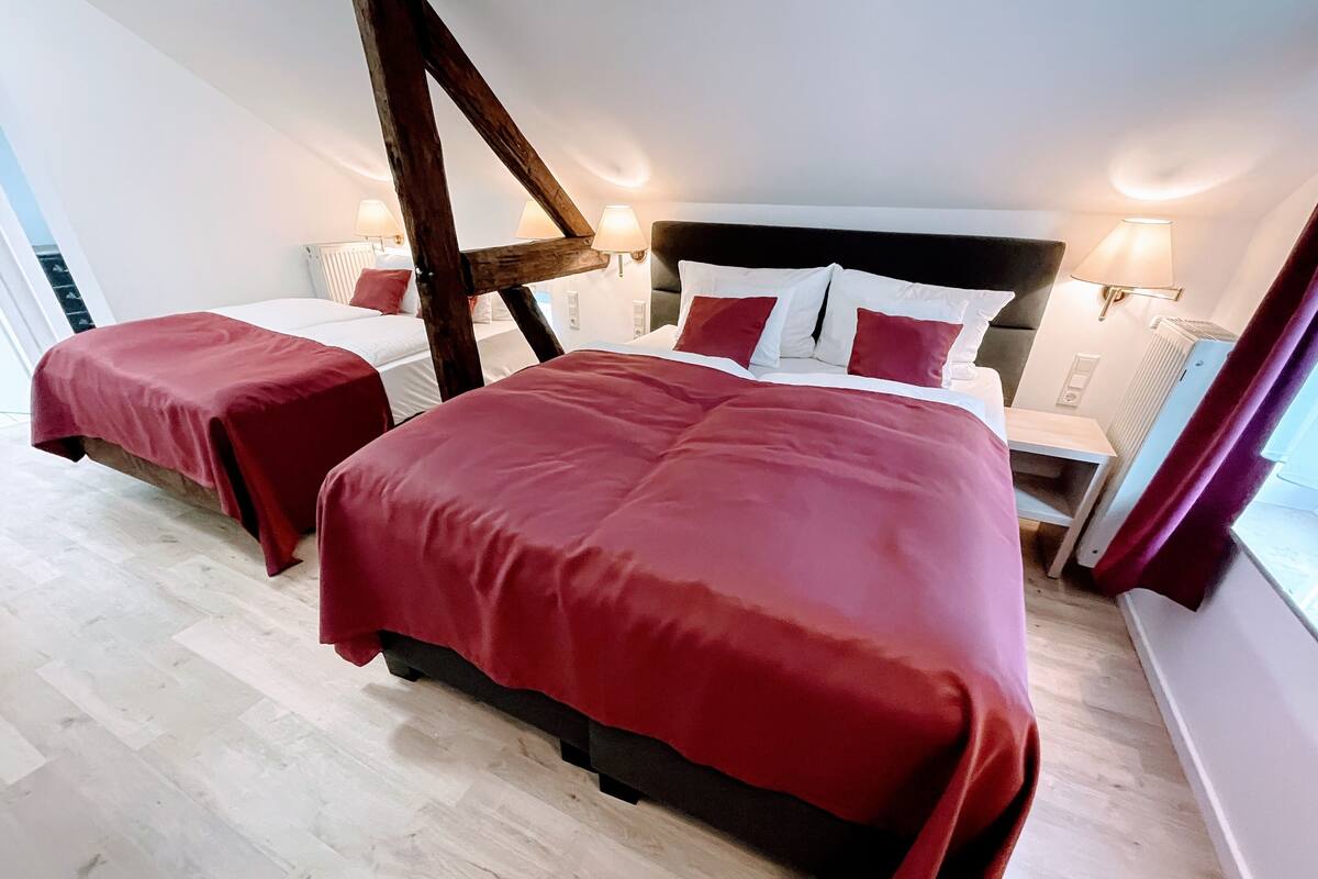 A bedroom with two beds, a wooden beam structure, and wall-mounted lamps.