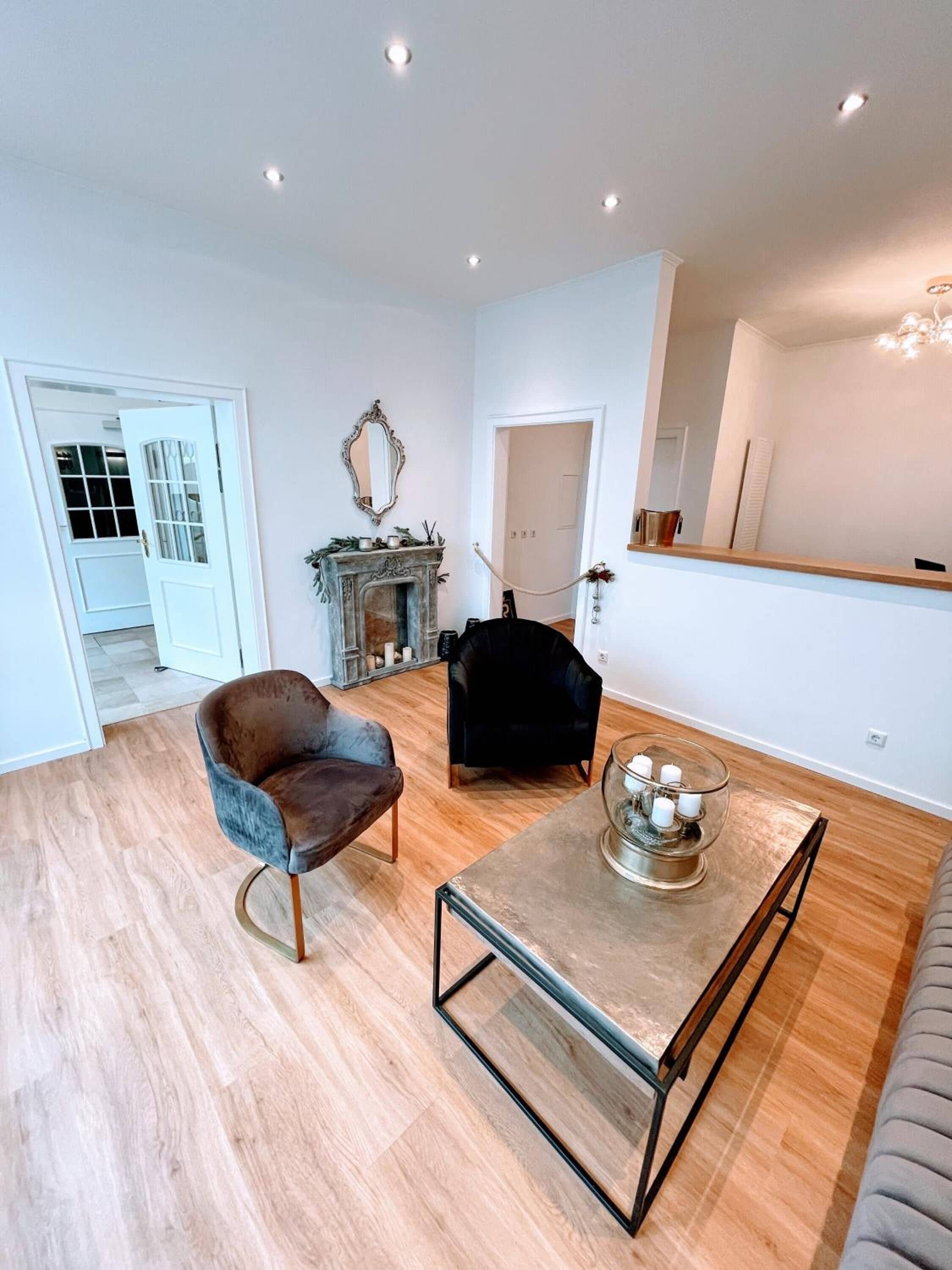 Un salón amplio con chimenea, dos sillones, una mesa de centro y un espejo grande en la pared.