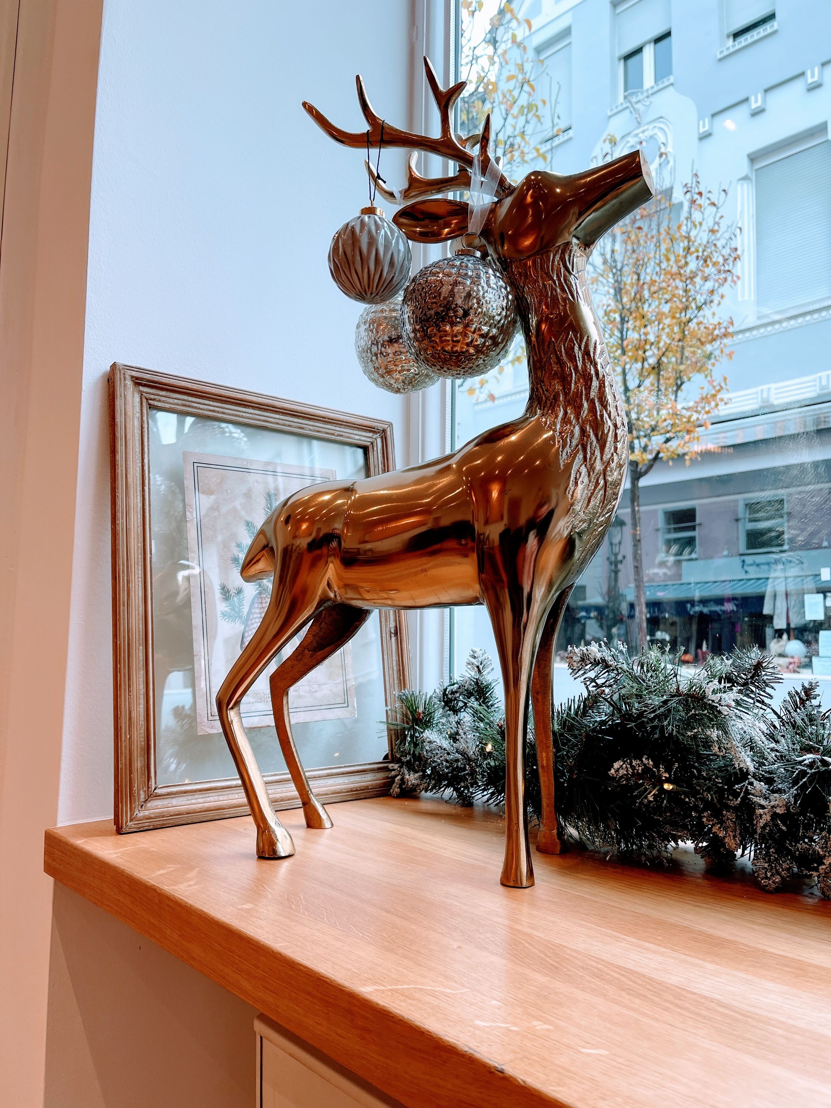 A metallic deer sculpture with antlers and a ball ornament on a wooden shelf.