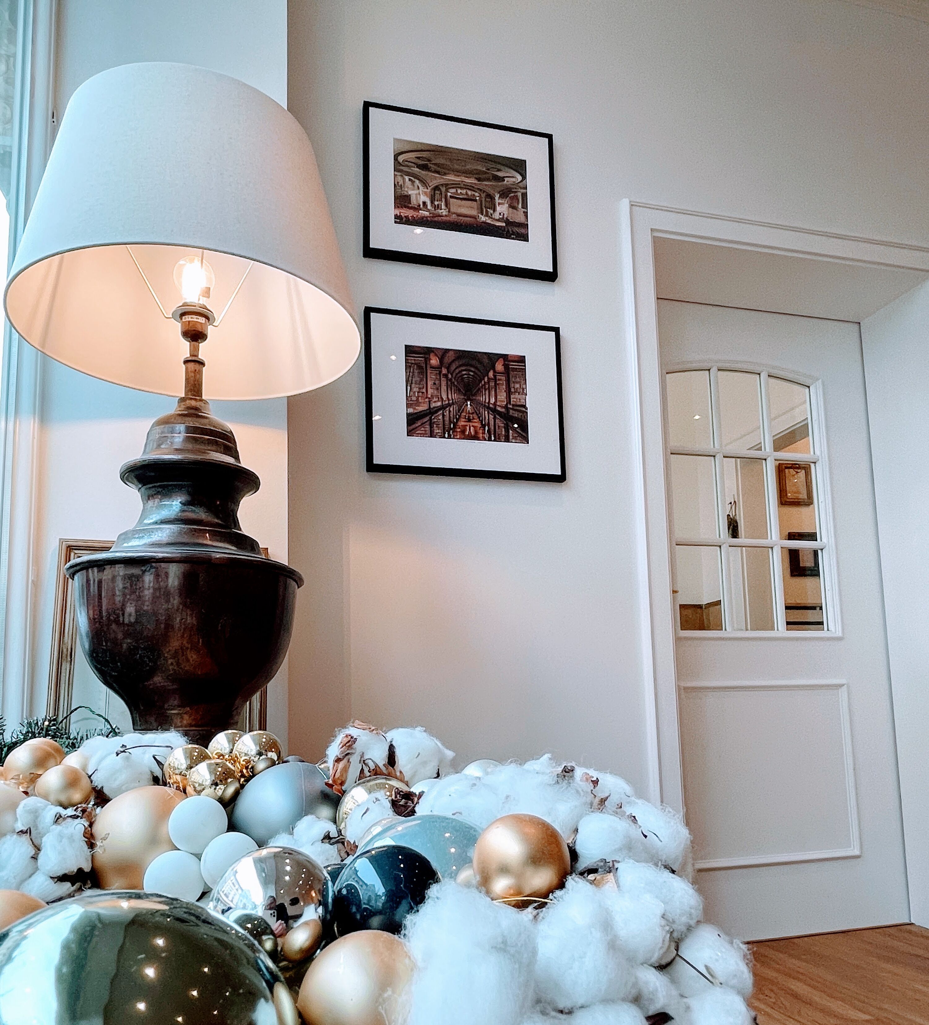 A room with a lamp, framed pictures on the wall, and a door with a window.