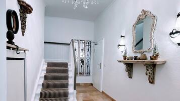 A hallway with a staircase, a chandelier, a mirror, and decorative wall elements.