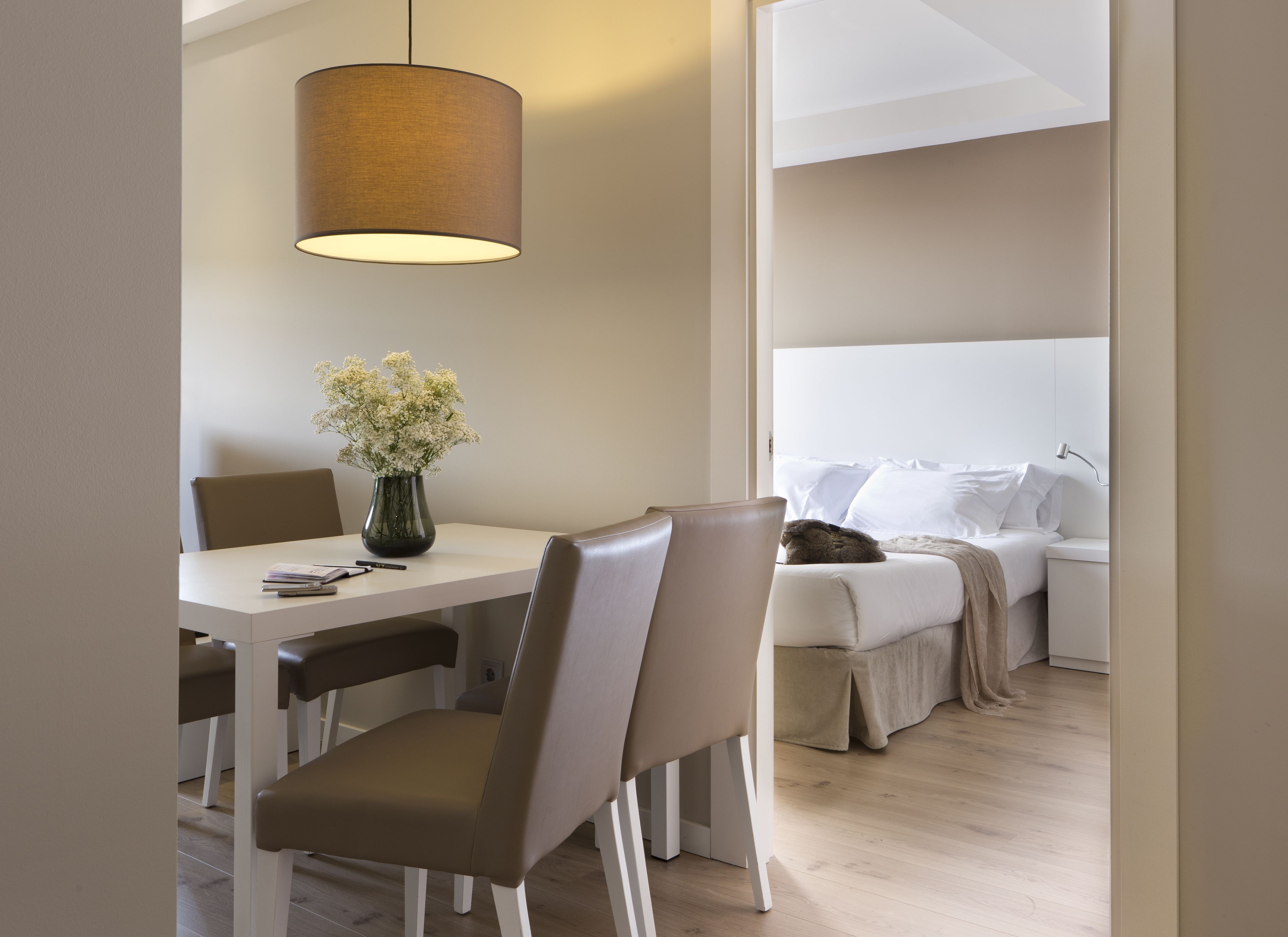 A modern hotel room with a dining area, a bed with white linens, and a hanging lamp.