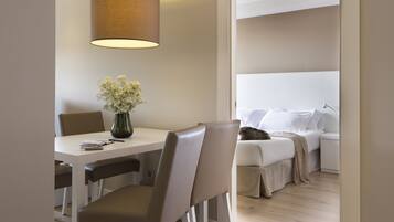 A modern hotel room with a dining area, a bed with white linens, and a hanging lamp.