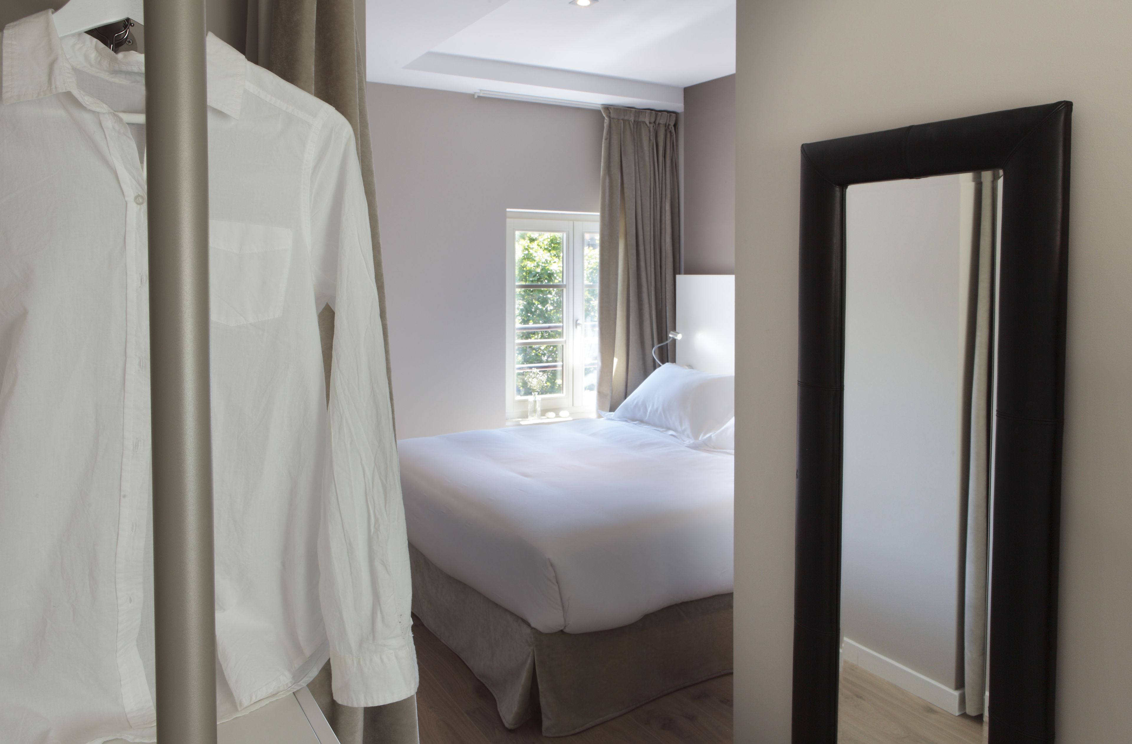 A hotel room with a bed, a hanging white shirt, and a door.
