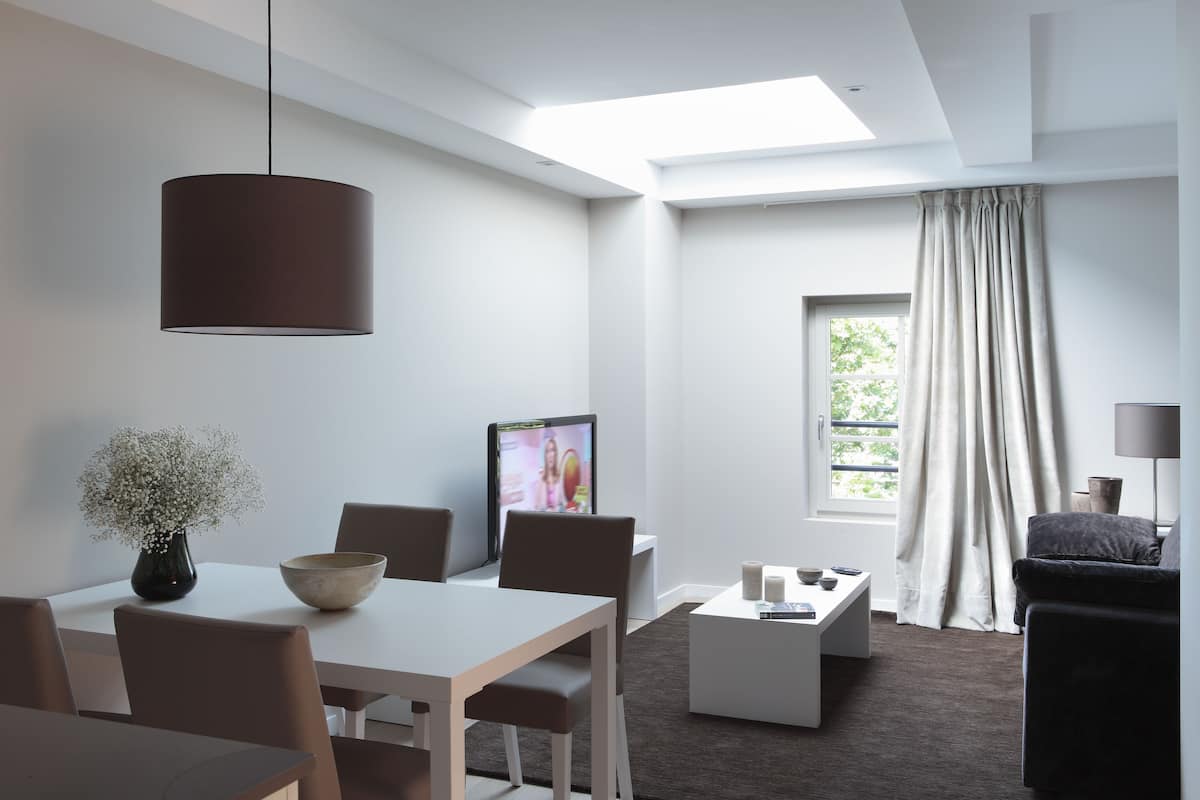 Un salon moderne comprenant un coin repas, un téléviseur à écran plat, une grande fenêtre avec des rideaux et un luminaire au plafond.