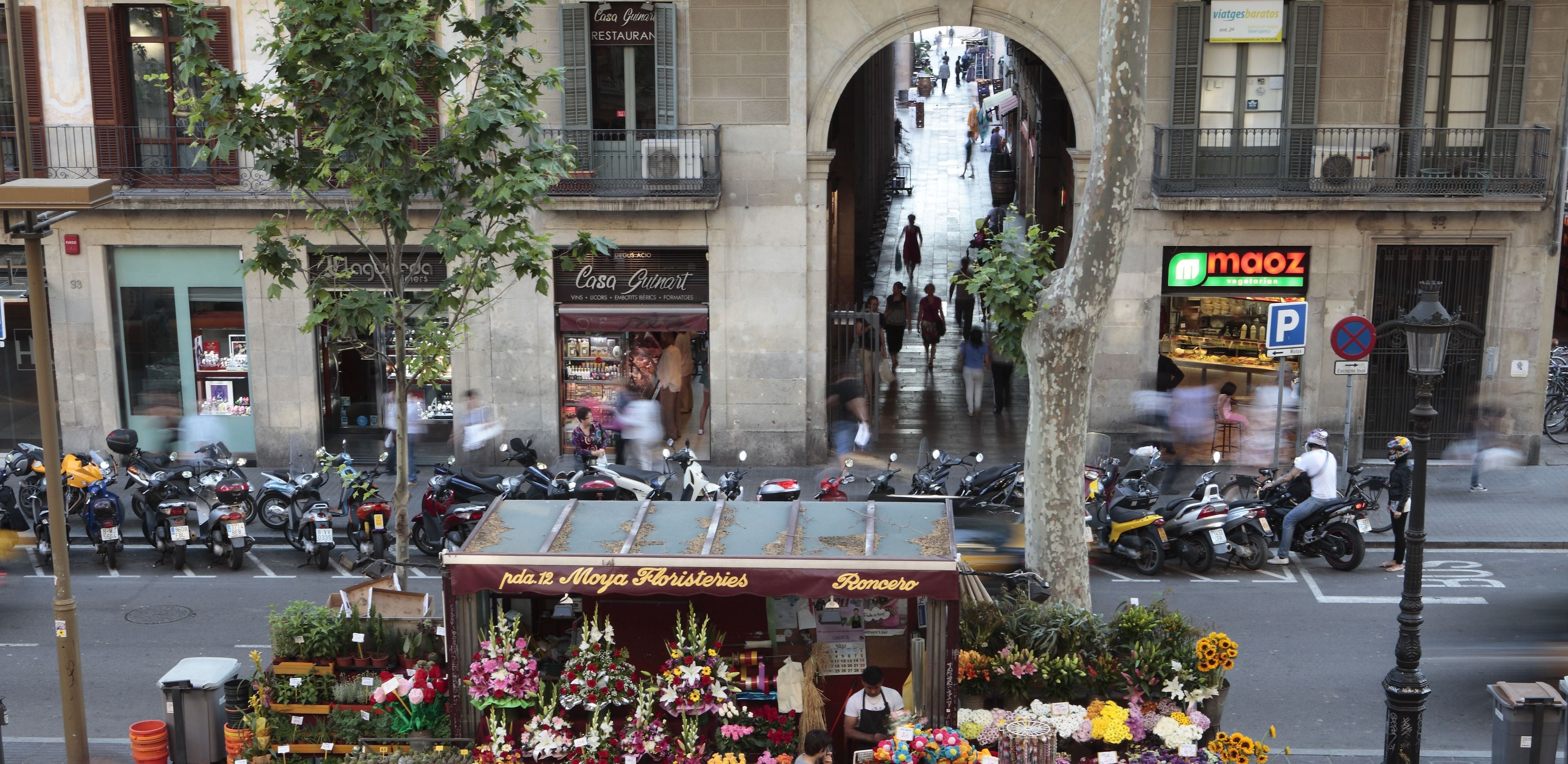 Vista de calle con una floristería, scooters estacionados y un restaurante.