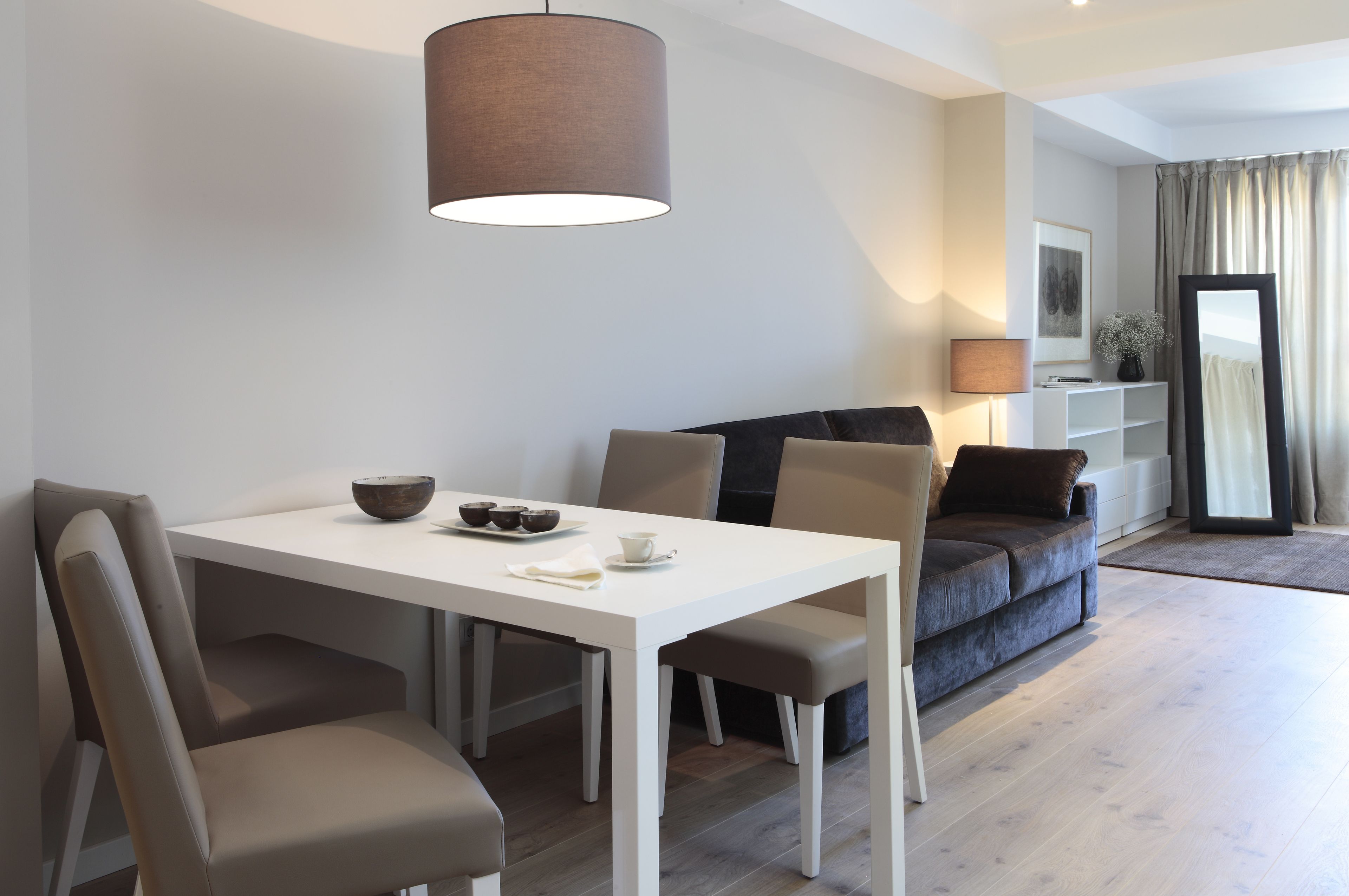 Un salon moderne avec une table à manger blanche, un canapé gris et une grande fenêtre agrémentée de rideaux.