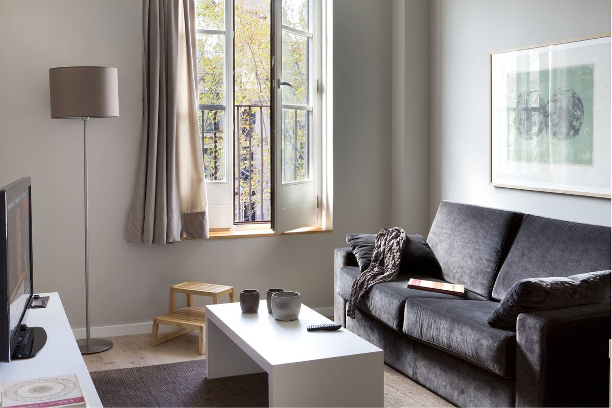 Un salon moderne avec un canapé gris, une table basse blanche, un lampadaire et une grande fenêtre avec des rideaux.