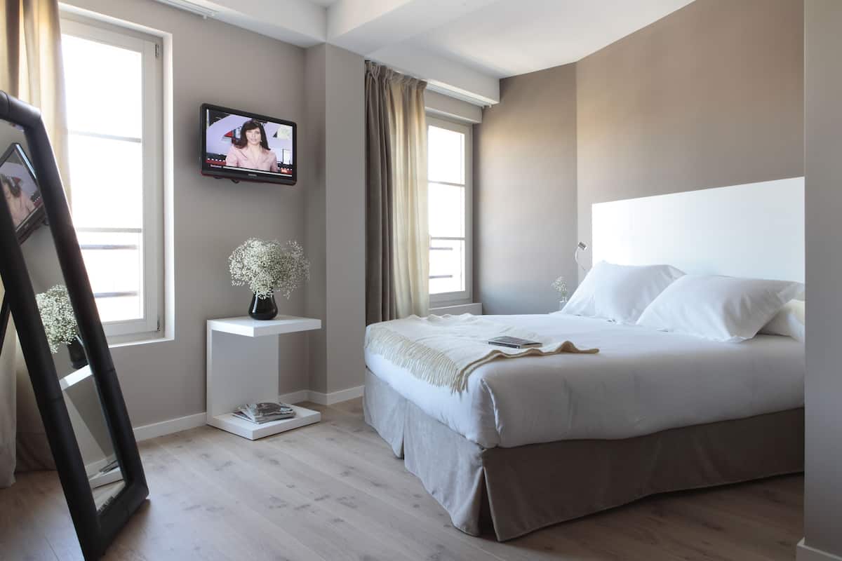 Une chambre à coucher moderne avec un grand lit, un téléviseur fixé au mur et une fenêtre avec des rideaux.
