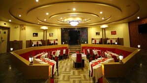 Un comedor amplio con varias mesas y cabinas, un candelabro central y piso alfombrado.