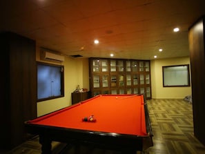 A pool table in a room with wooden flooring and a cabinet with glass doors.