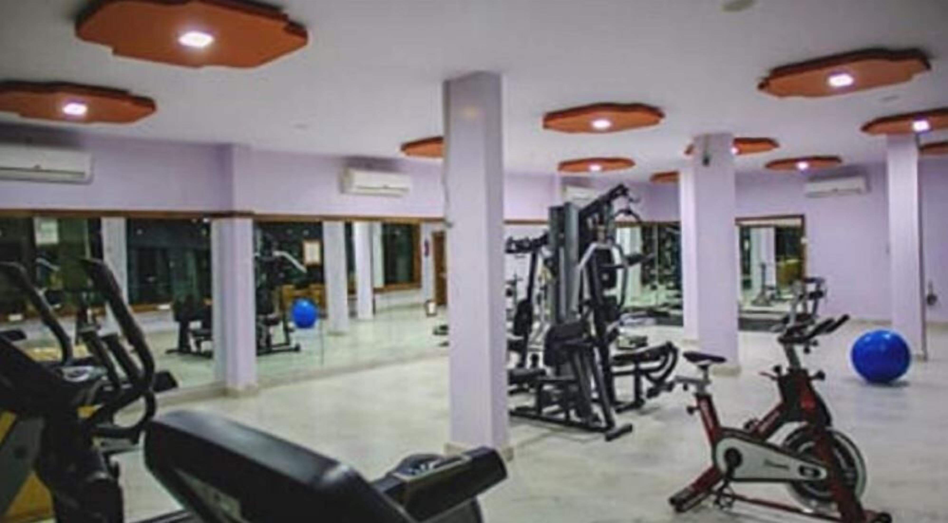 A gym with various exercise equipment, including treadmills and weight machines, and a large mirror wall.
