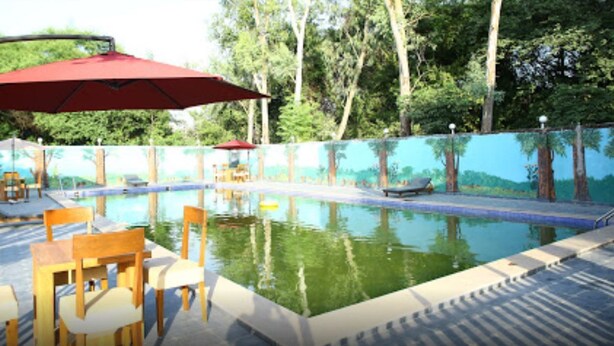 Una piscina con sillas y mesas de madera, rodeada por una valla con un mural.