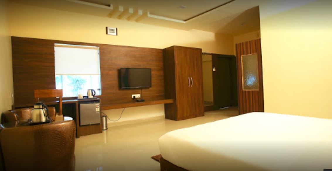 Una habitación de hotel con cama, televisor montado en la pared, escritorio con silla y armario.