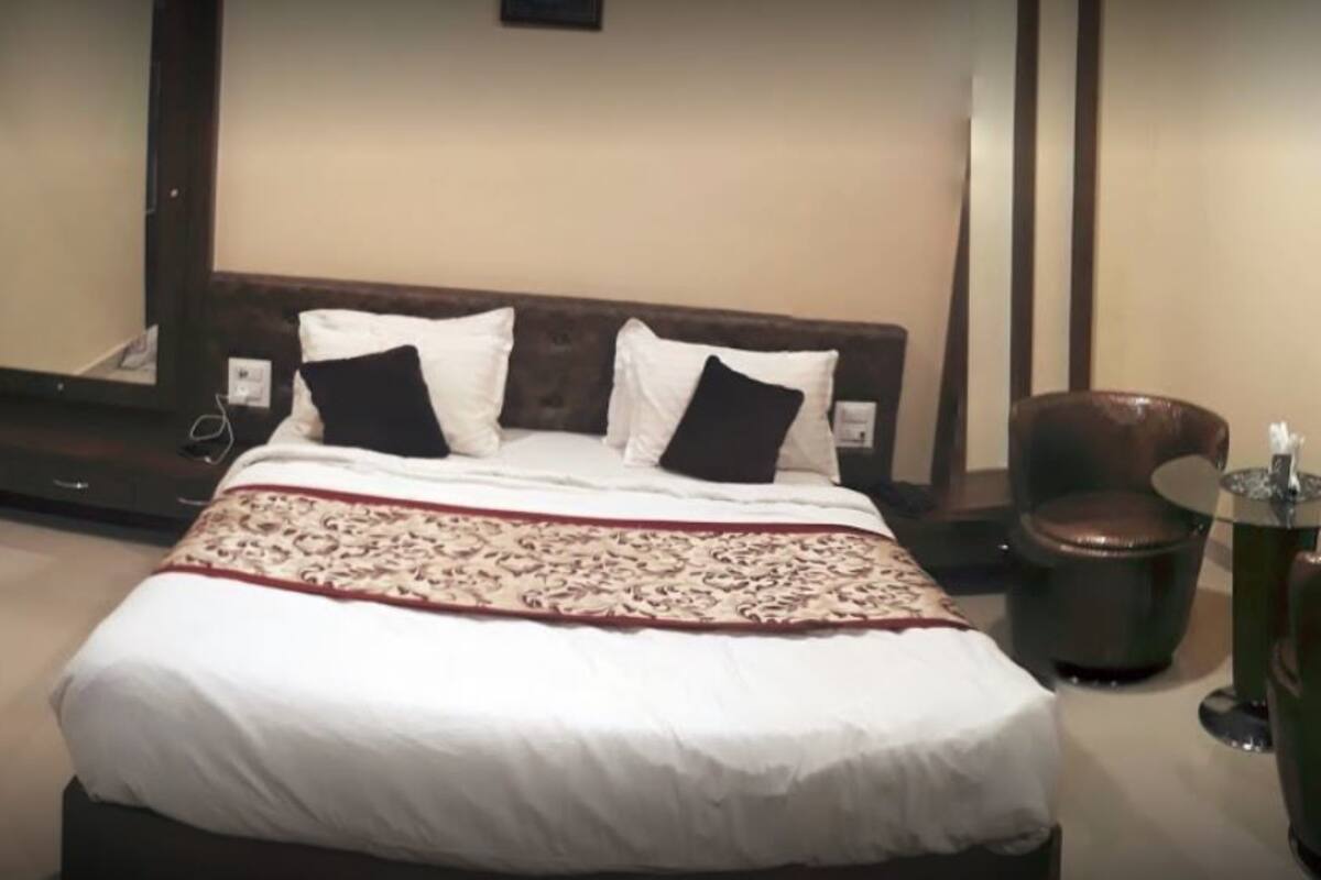 A hotel room with a large bed, a wooden headboard, a mirror, a round table with chairs, and a small trash bin.