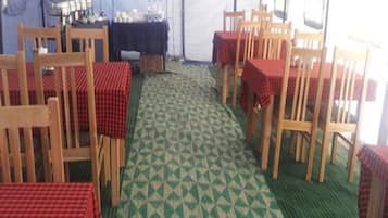 A tented dining area with tables covered in red checkered tablecloths, wooden chairs, and a patterned carpet.