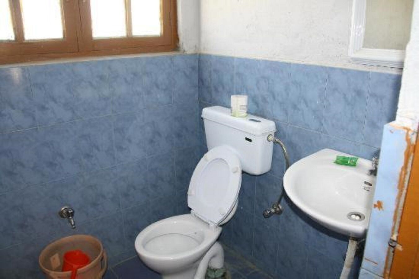 A small bathroom with blue walls, a white toilet, a sink, and a window.