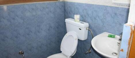 A small bathroom with blue walls, a white toilet, a sink, and a window.