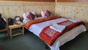 Ein Hotelzimmer mit einem holzverkleideten Kopfteil, einem Bett mit weißer und roter Bettwäsche, einem Nachttisch mit Tasche und Wasserflasche sowie einem grünen Teppich.