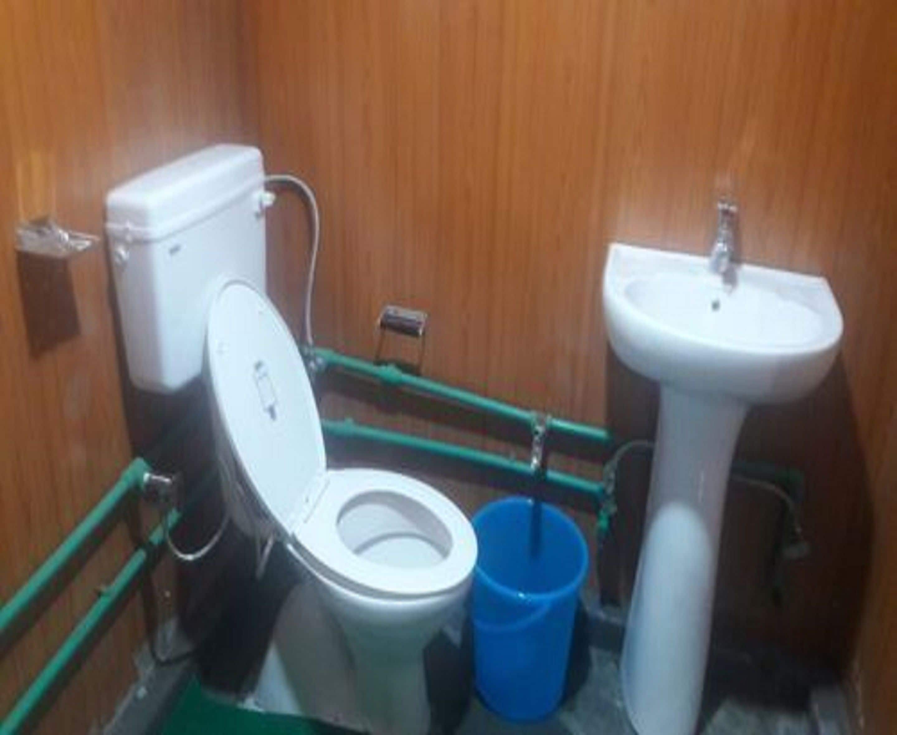 A small, compact bathroom with a toilet, a sink, and a blue bucket.
