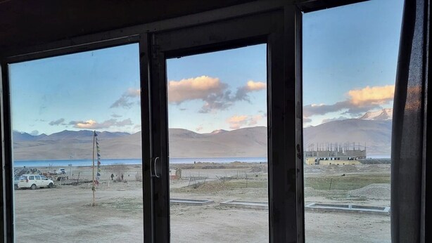Ein Fenster mit Blick auf eine Baustelle, ein Gewässer und ferne Berge.