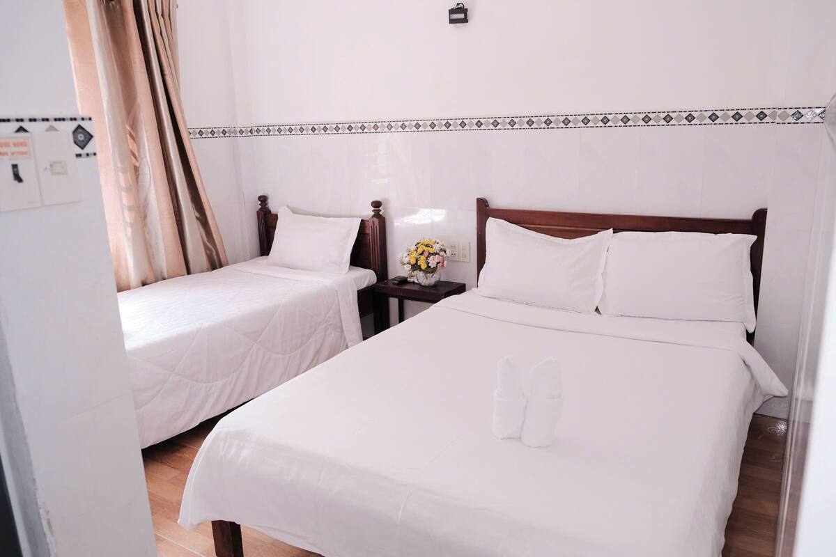 Une chambre d’hôtel avec deux lits simples, une table de chevet ornée d’un vase de fleurs et un motif décoratif sur le mur.