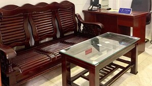 A waiting area with a wooden bench, a glass-top table, a desk with a computer, and a wall-mounted decorative piece.