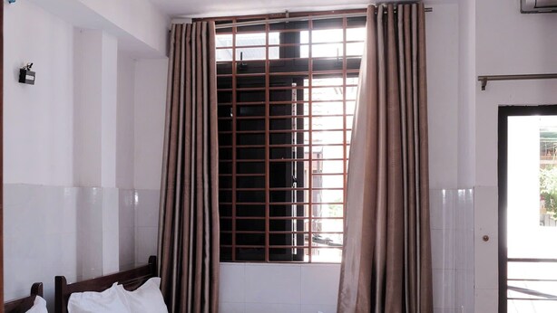 A hotel room with two beds, a window with curtains, and an air conditioning unit on the wall.
