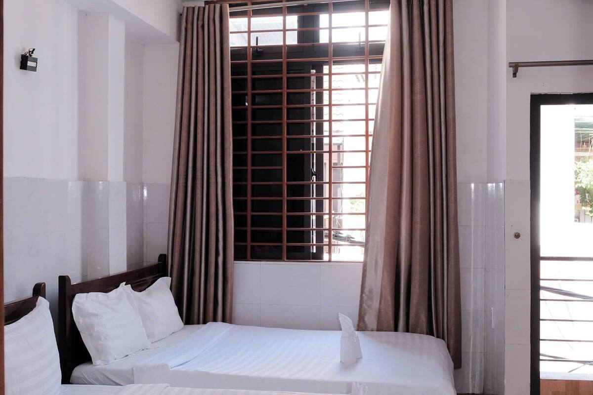 Une chambre d’hôtel avec deux lits, une fenêtre avec des rideaux et un climatiseur fixé au mur.