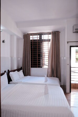 Una habitación de hotel con dos camas, una ventana con cortinas y un equipo de aire acondicionado en la pared.