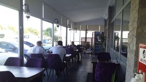 An outdoor cafe with tables and chairs, a car parked outside, and a sign on the wall. - Udi Hotel (Çanakkale)
