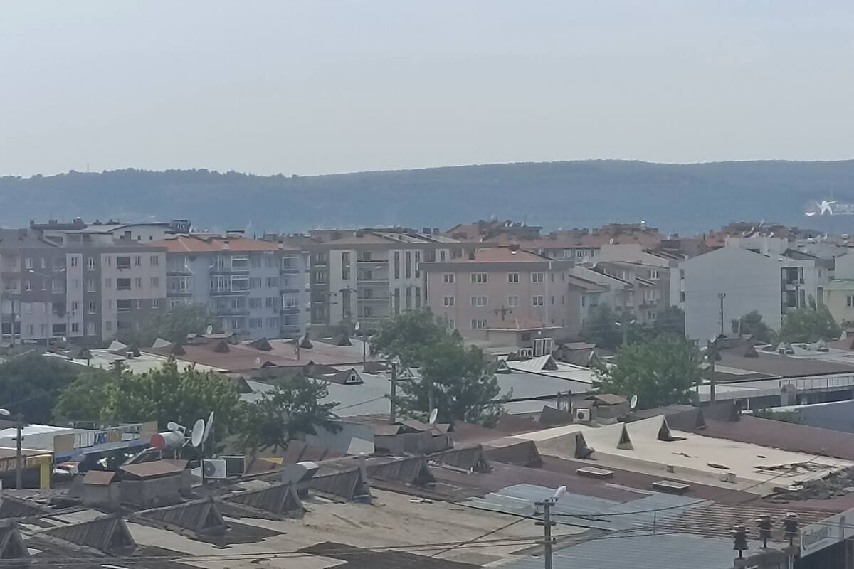 A residential area with multi-story buildings, some with satellite dishes, and a hilly landscape in the background.