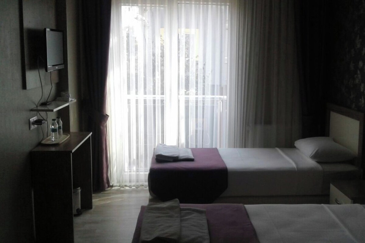 A hotel room with a bed, a bedside table, a TV, and a window with curtains.