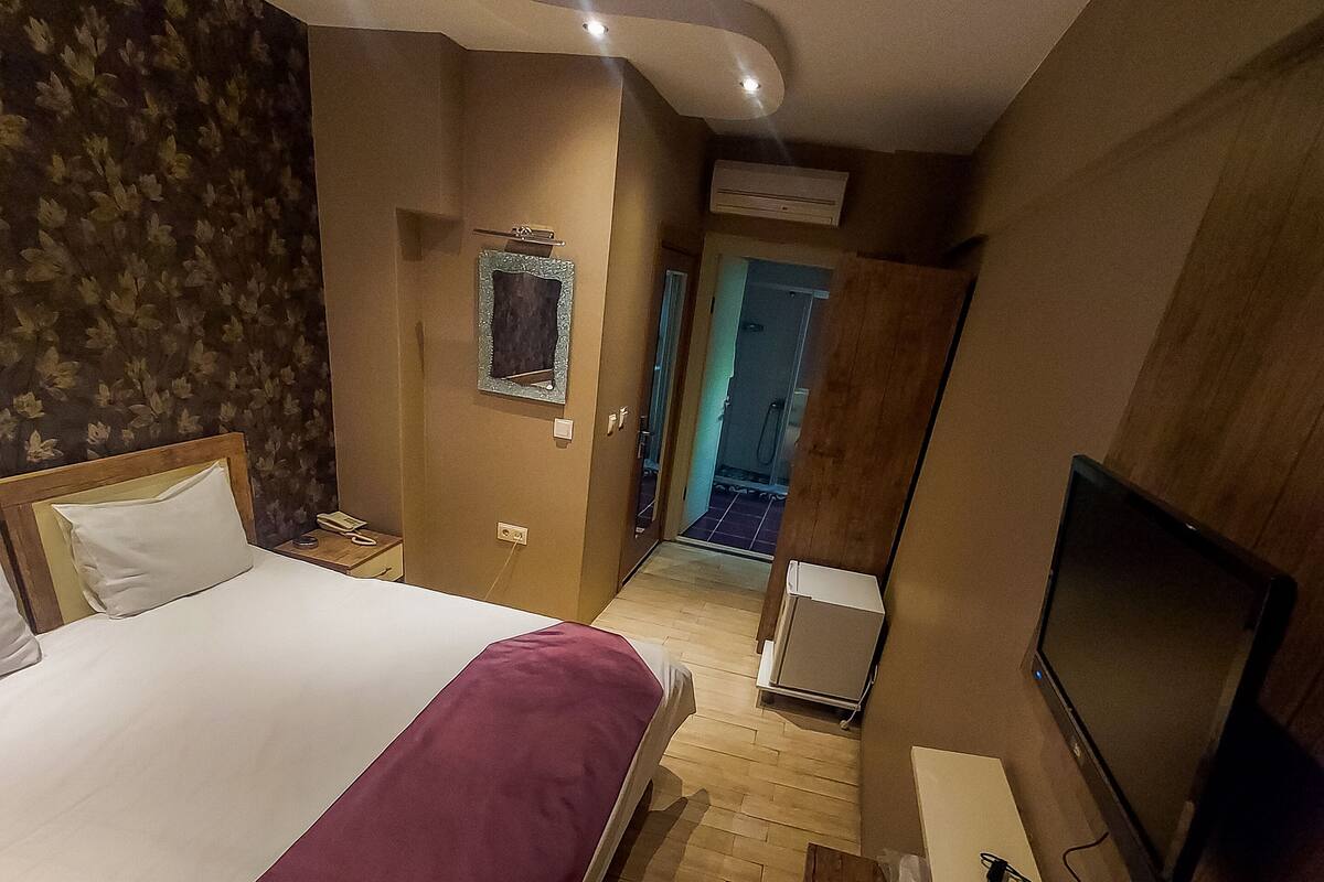 A hotel room with a large bed, a desk with a computer and a TV, a bathroom visible through an open door, and a mirror on the wall.