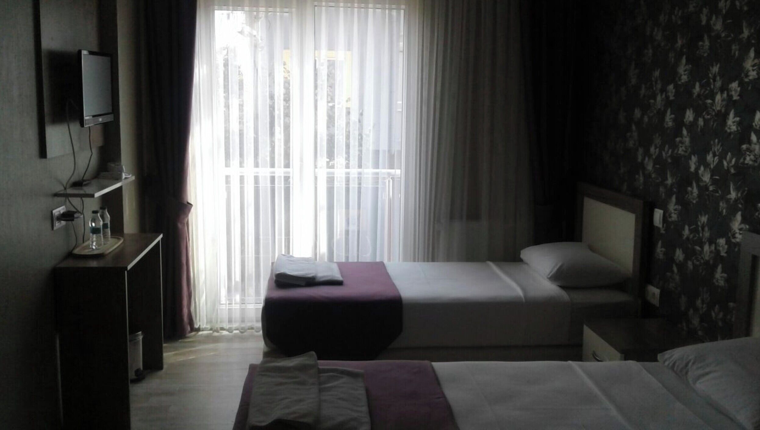 A hotel room with a bed, a bedside table, a TV, and a window with curtains.