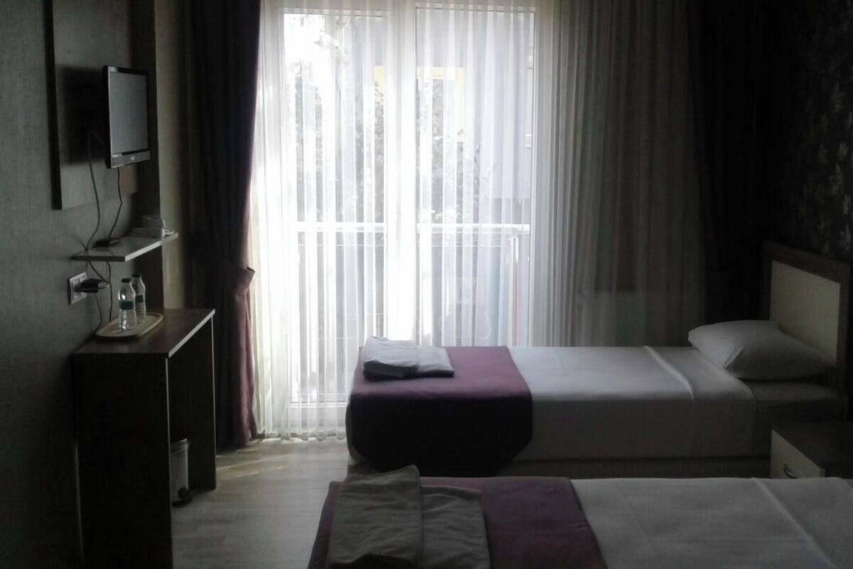 A hotel room with a bed, a bedside table, a TV, and a window with curtains.
