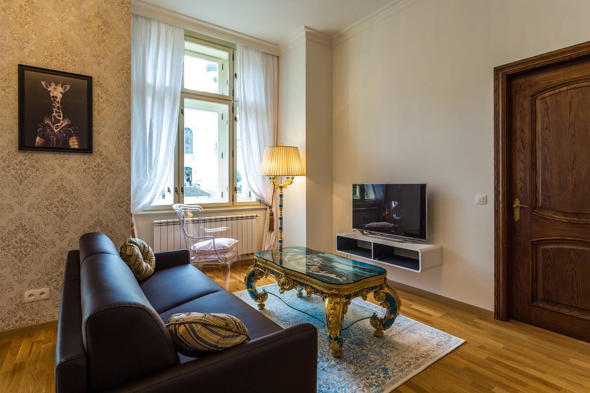 A living room with a sofa, a glass coffee table, a lamp, a TV, and a wooden door.