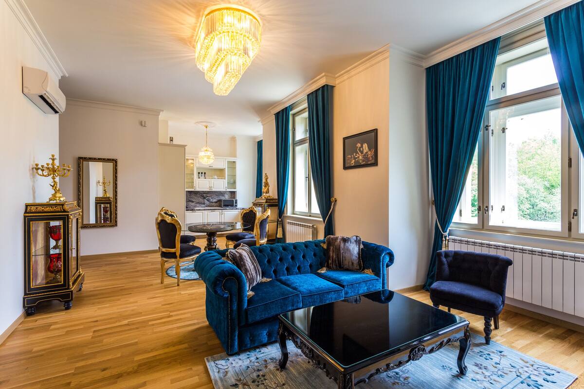 A spacious living room with a blue sofa, a black coffee table, and a chandelier.