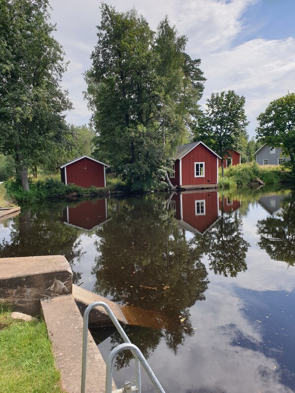 A calm water body with red buildings reflecting on the surface, surrounded by greenery.