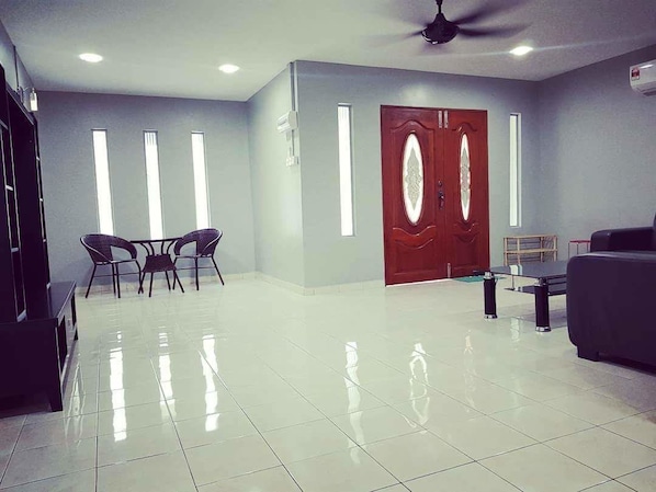 A spacious lobby with a polished tile floor, a dark-colored sofa, a wooden door with glass panels, and a ceiling fan.
