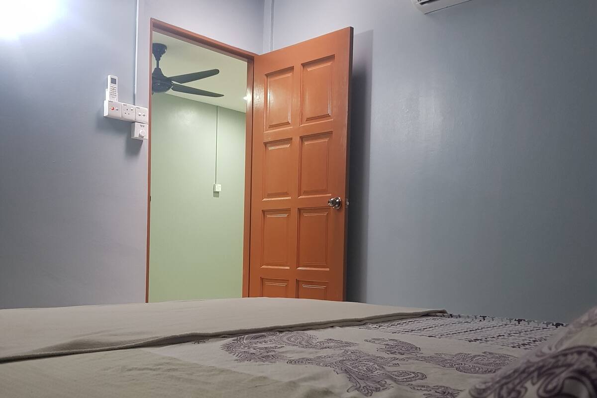 A bedroom with a bed, an air conditioner, a ceiling fan, and a door.