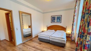 A hotel room with a wooden floor, a double bed with a headboard, a large mirror, and a picture on the wall. - Kurhaus Nordstrand - Apartment 45407 - KH - Apartment 38 (Göhren)