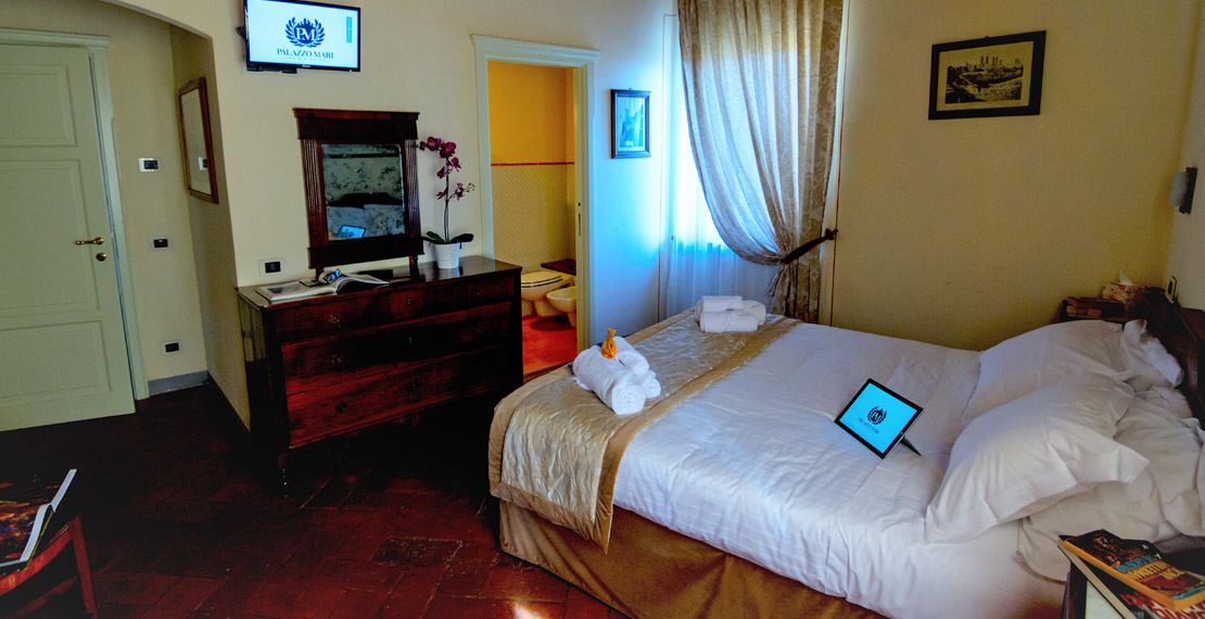 A hotel room with a bed, a desk with a computer, a TV, and a bathroom visible through an open door.